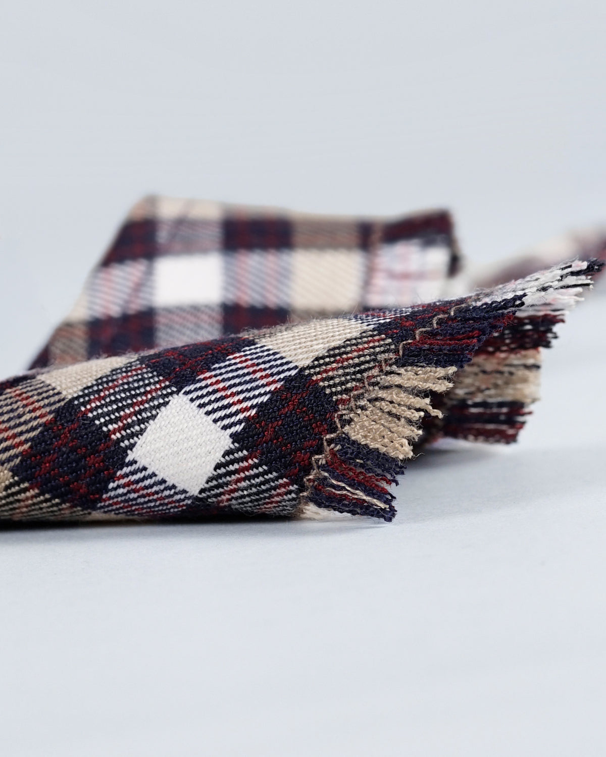 Close-up of an aubergine checked bandana showing the woven check and fringed edge