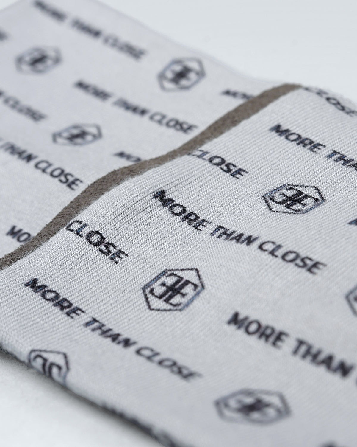 Close-up of the snood fabric, the wordmark and small hexagon logo printed across a soft grey knit