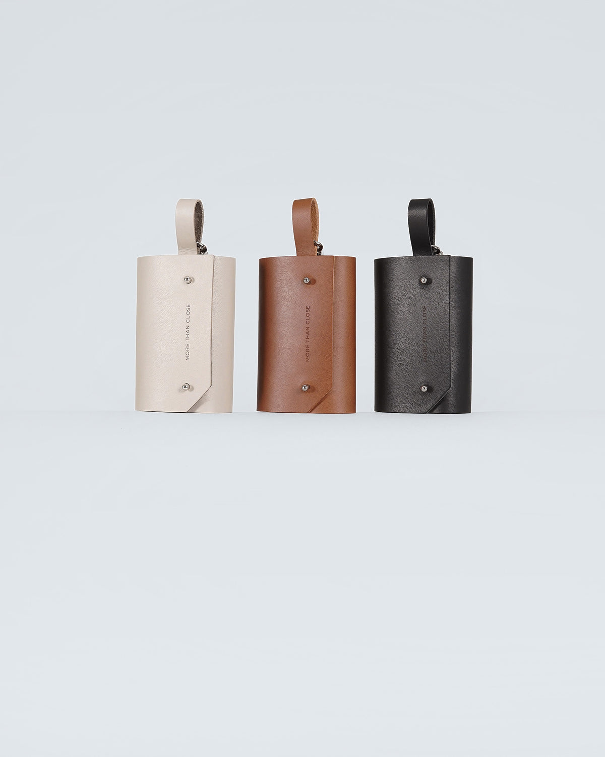 Leather poop bag holders in greige, chestnut and black, side by side