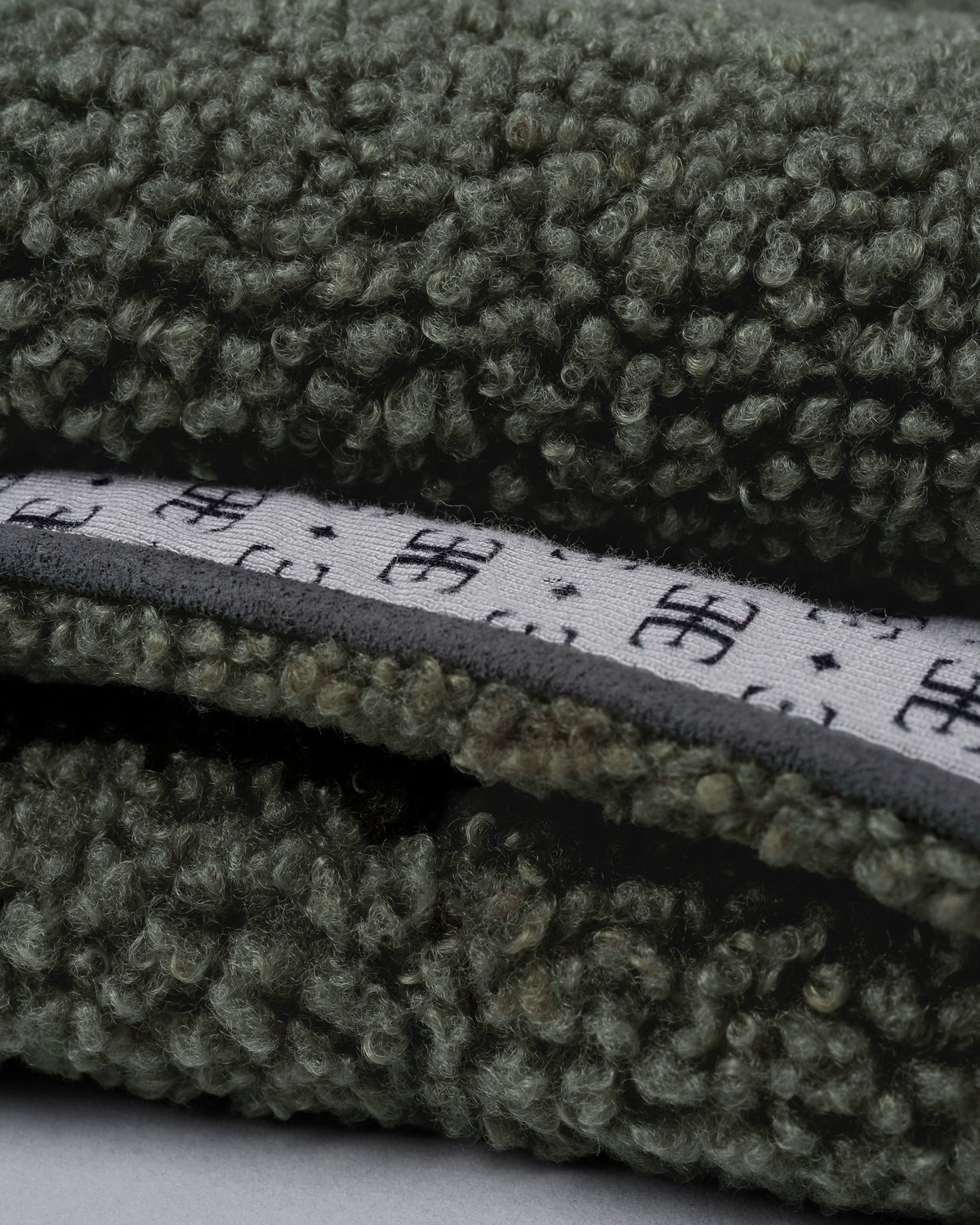 Close-up of a forest green bouclé dog blanket edge with faux-suede piping and patterned lining