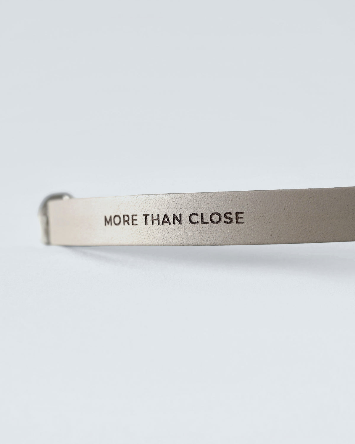 Close-up of the greige leather strap with the brand line embossed along its narrow width