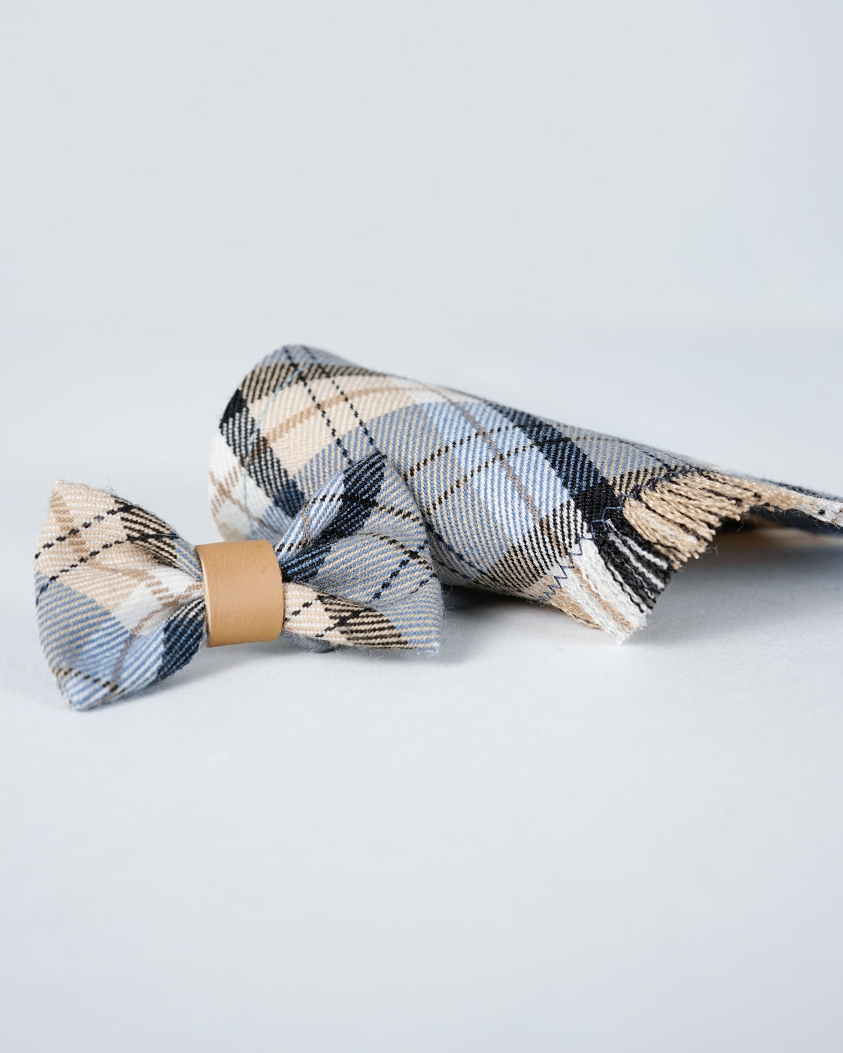 Light blue checked dog scarf folded beside a matching bow with a leather centre