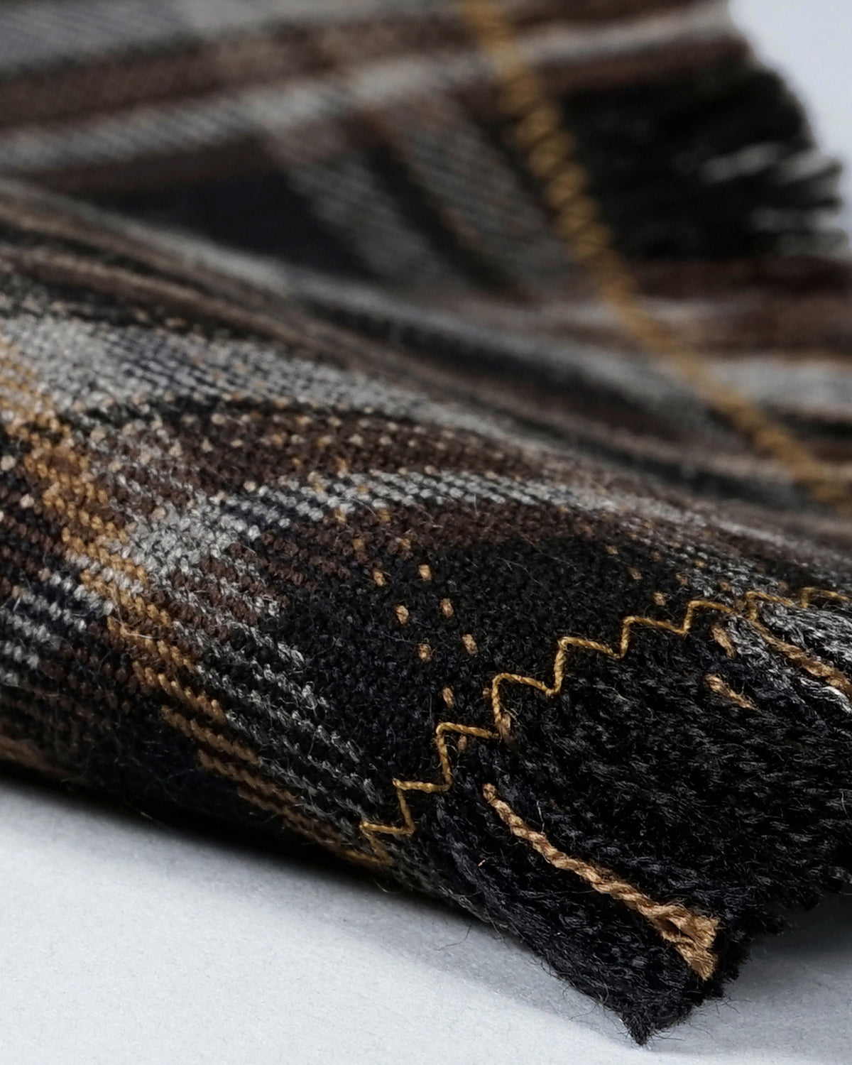 Close-up of the black checked fabric, showing the woven pattern, gold zigzag stitching and cut fringe