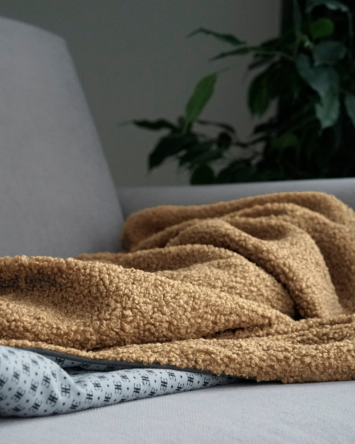 Camel bouclé blanket for dogs draped over a sofa, with its patterned lining showing