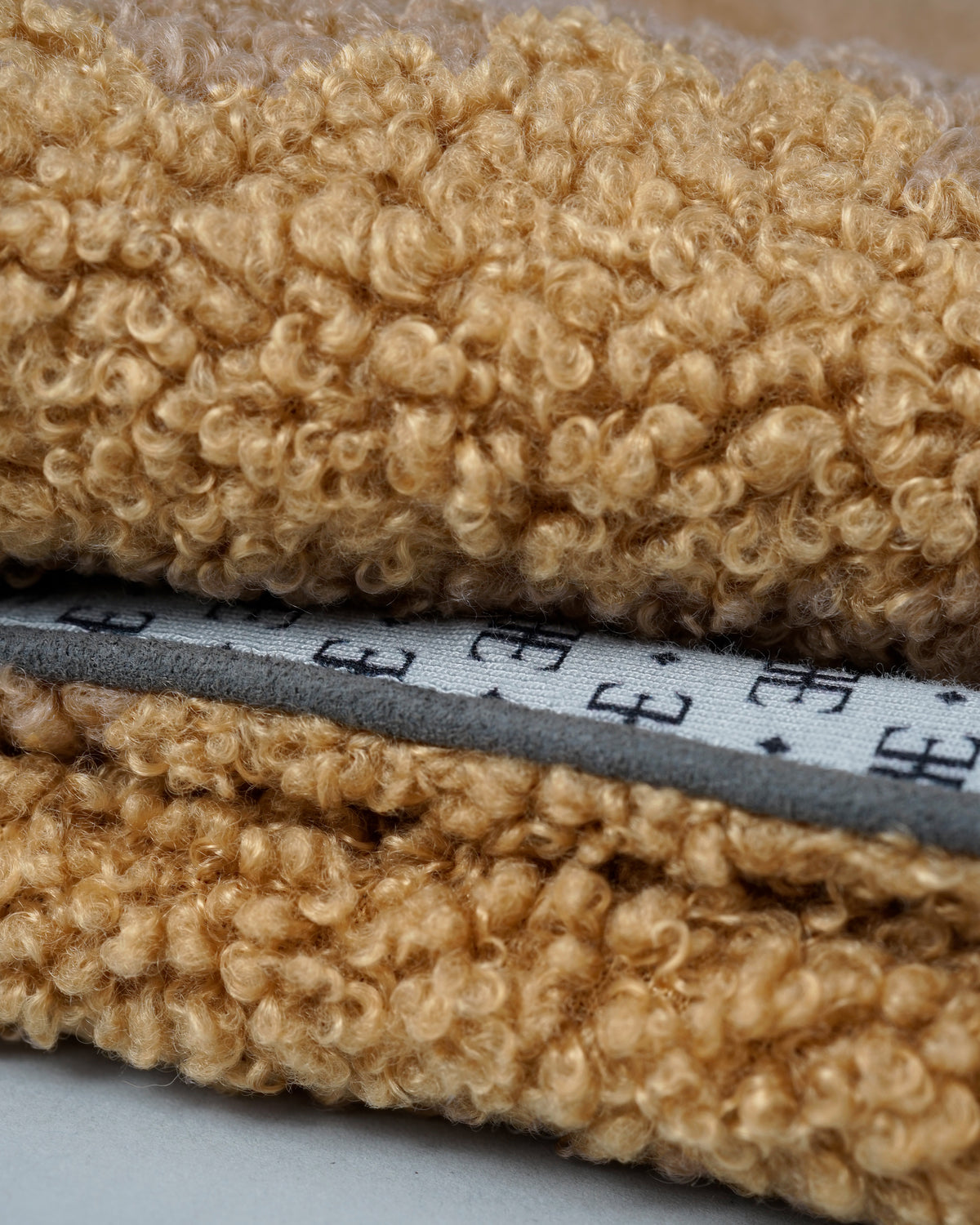 Close-up of a camel bouclé dog blanket with faux-suede piping and patterned lining