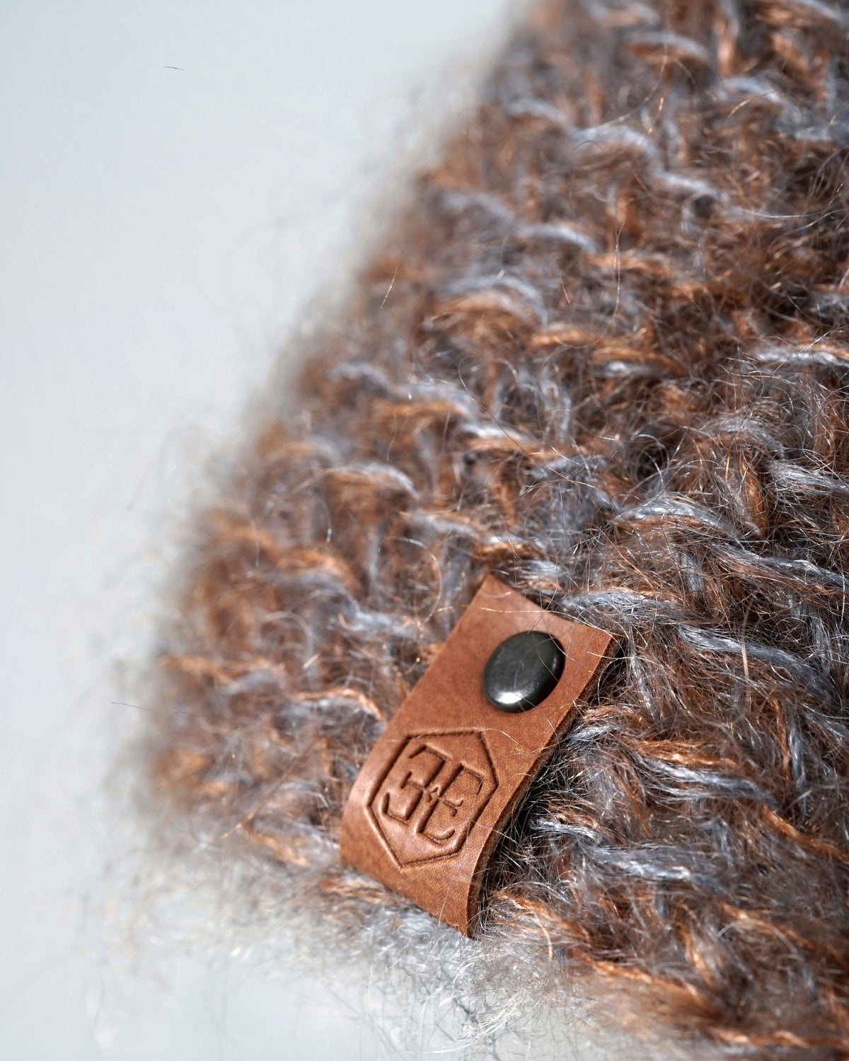 Close-up of the blue brown melange knit, with a stamped leather tab held by a dark metal stud at the edge
