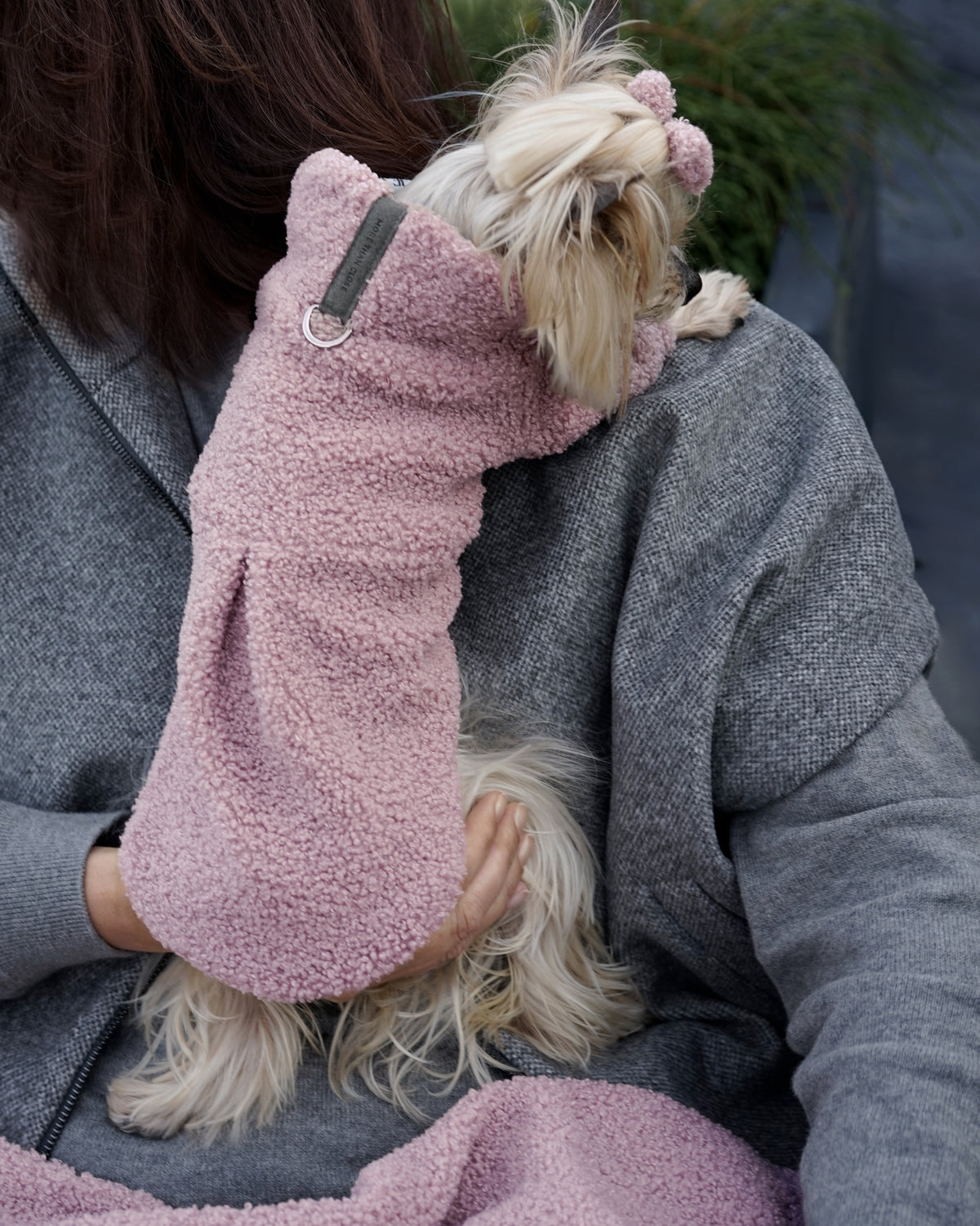 Back view of a small cream dog being held over a shoulder in a powder pink bouclé dress
